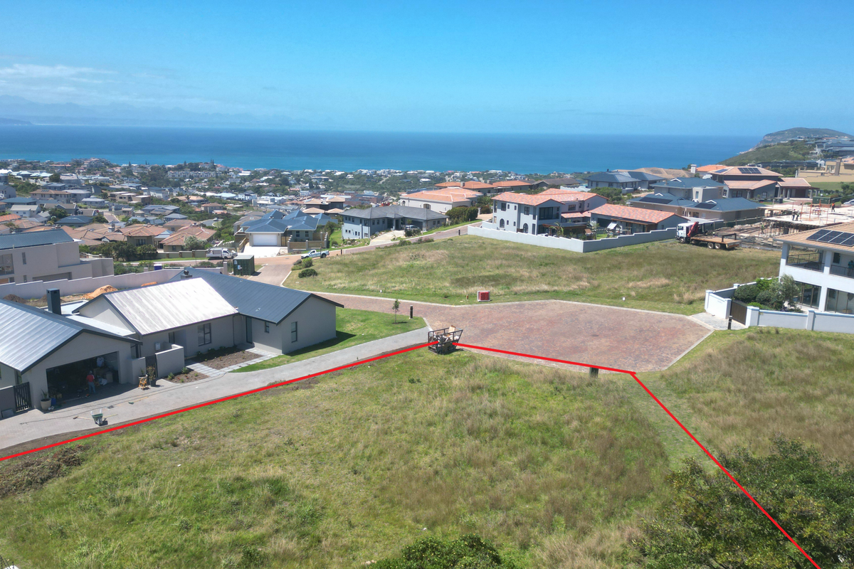 An aerial view of a vacant residential plot featuring a paved driveway and clear boundary lines, set within a developed coastal estate.