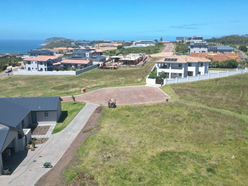 Aerial view of a residential vacant land plot within a developed coastal estate, featuring paved access and surrounding established homes.