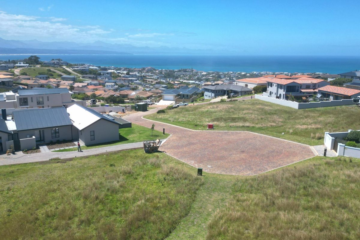Aerial view of a vacant residential plot featuring a paved driveway, situated in a coastal estate with panoramic ocean and mountain views.