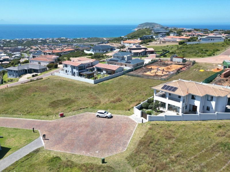 Aerial view of a vacant residential plot in a coastal estate, featuring established surrounding homes and paved access.