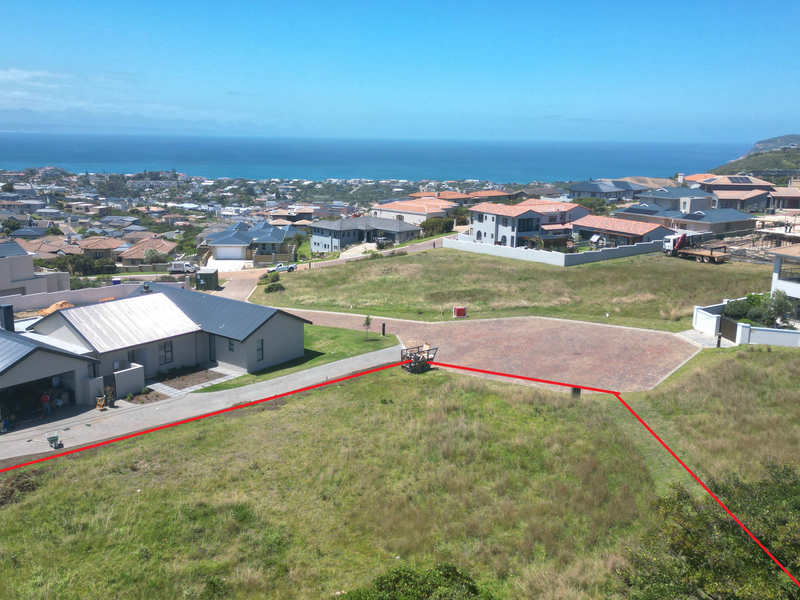 An aerial view of a vacant residential plot featuring a paved driveway and clear boundary lines, set within a developed coastal estate.