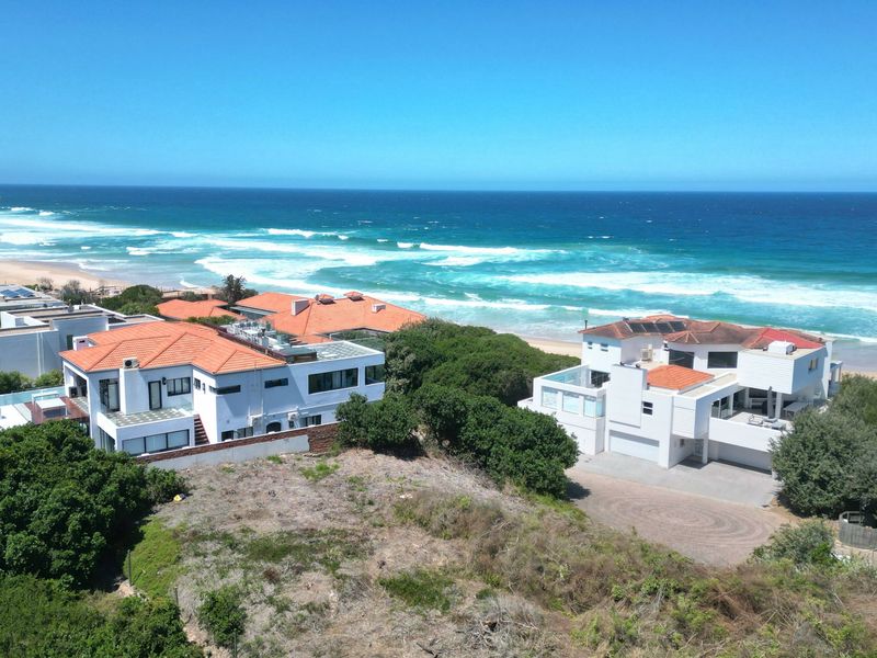 An aerial view of a coastal residential area featuring beachfront properties with direct ocean access and scenic sea views.