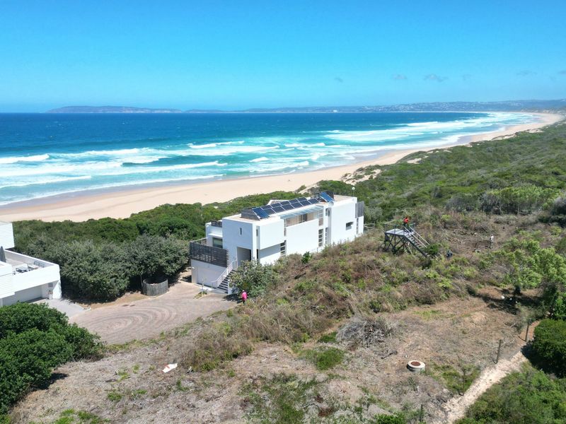 Aerial view of a coastal residential property featuring solar panels, surrounded by natural vegetation with direct proximity to the beach and ocean.