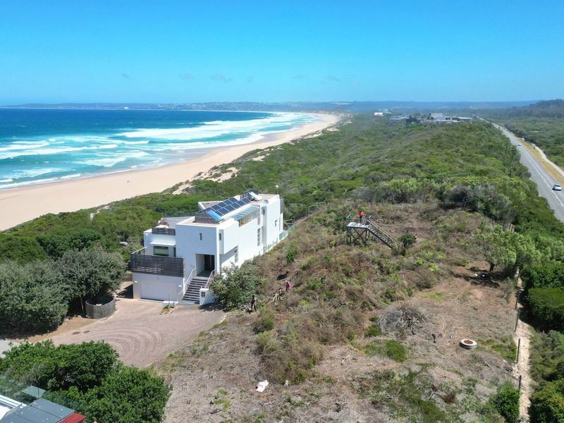 Aerial view of a coastal residential property featuring a modern home, solar panels, and direct proximity to the beach and main road.