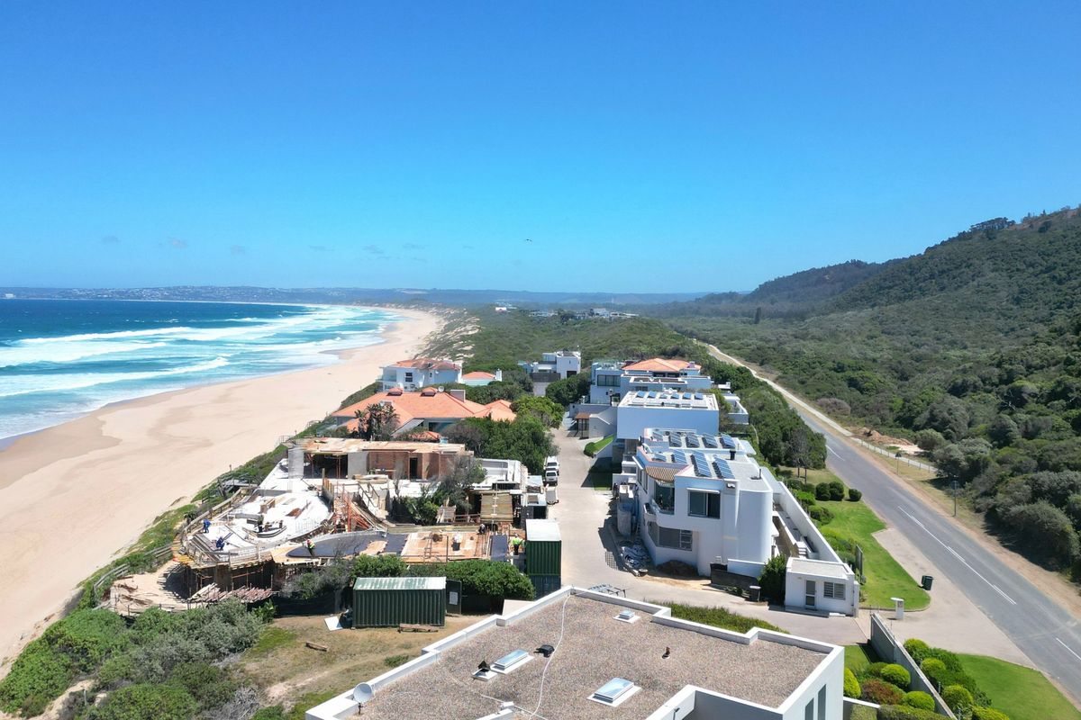 Aerial view of a coastal residential development situated along the beach, featuring modern homes with solar installations and direct access to the coastline.