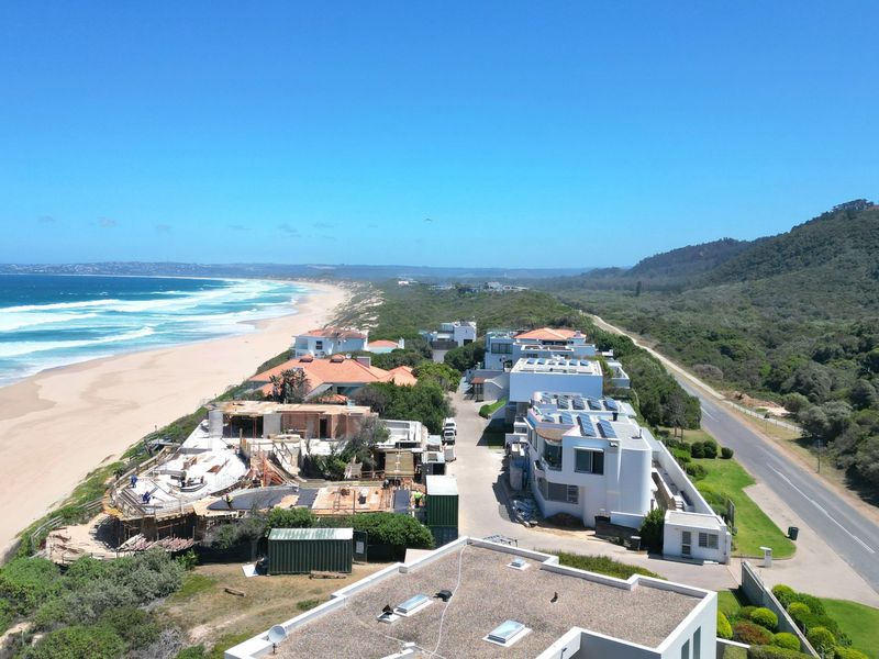 Aerial view of a coastal residential development situated along the beach, featuring modern homes with solar installations and direct access to the coastline.