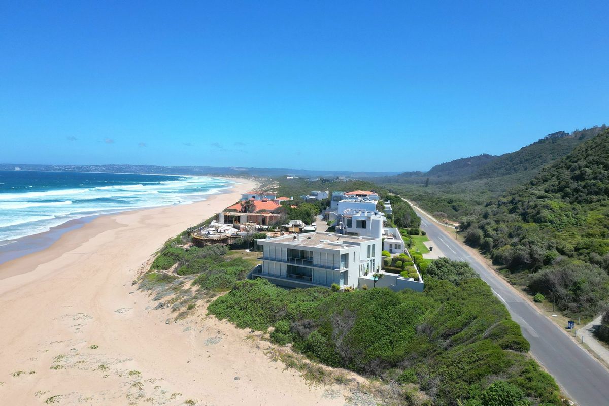 An aerial view of a coastal residential property situated directly along the beach, featuring proximity to the ocean and surrounding natural landscape.