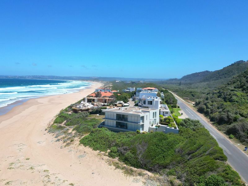 An aerial view of a coastal residential property situated directly along the beach, featuring proximity to the ocean and surrounding natural landscape.