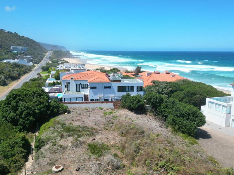 Aerial view of a coastal residential area featuring vacant land, nearby homes, and direct proximity to the ocean and beach.
