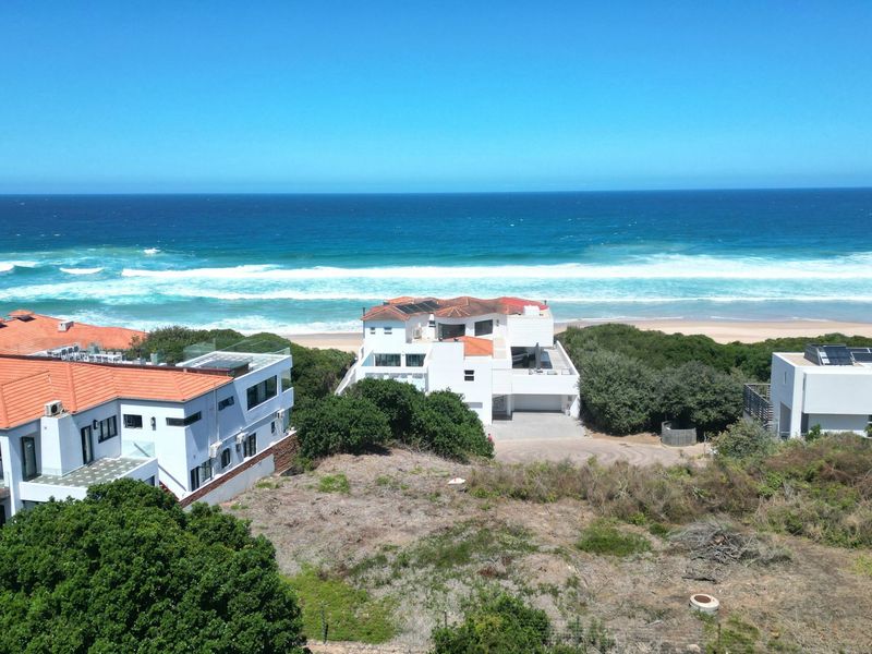 An aerial view of a residential coastal plot featuring surrounding homes and direct ocean views.
