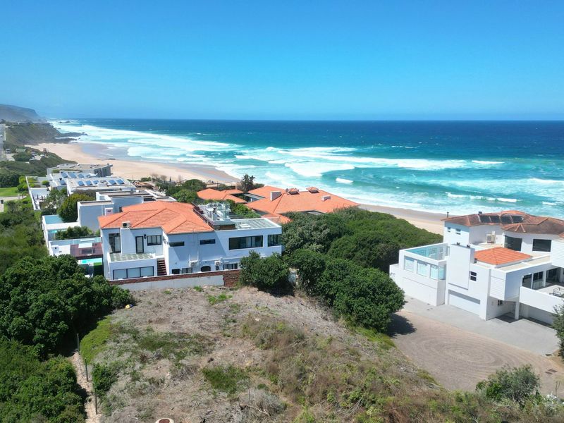 An aerial view of a coastal residential area featuring beachfront properties, proximity to the ocean, and surrounding natural landscape.