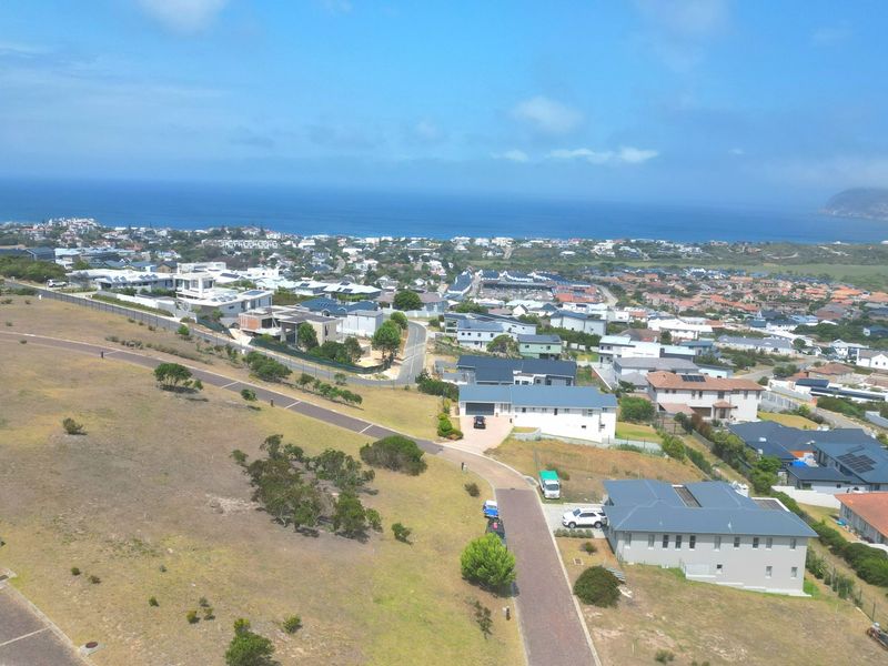 An aerial view of a residential estate featuring vacant land plots, paved roads, and established homes with coastal views in the background.