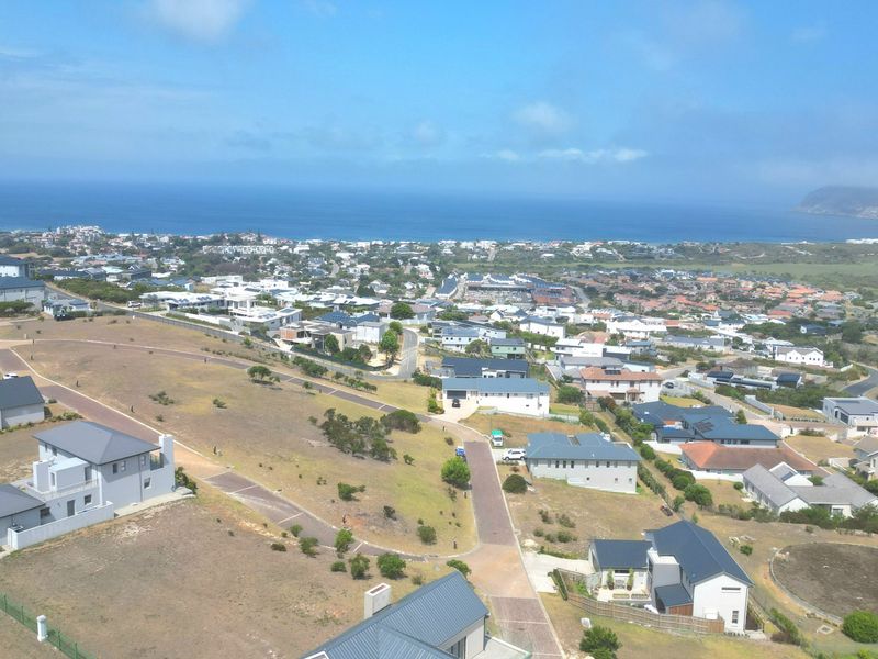 An aerial view of a residential estate featuring vacant plots, paved roads, and surrounding coastal landscape.