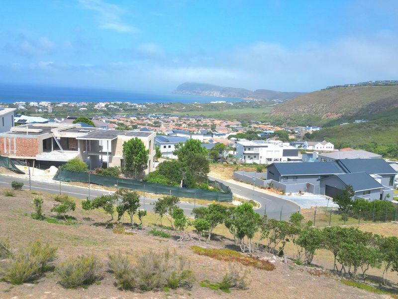 Elevated panoramic view overlooking a coastal residential estate, surrounding hills, and the ocean in the distance.