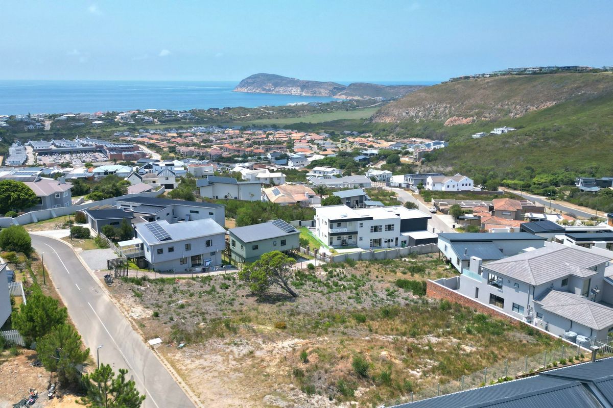 An aerial view of a vacant residential plot situated within a developed coastal neighborhood, offering scenic views of the surrounding landscape and ocean.