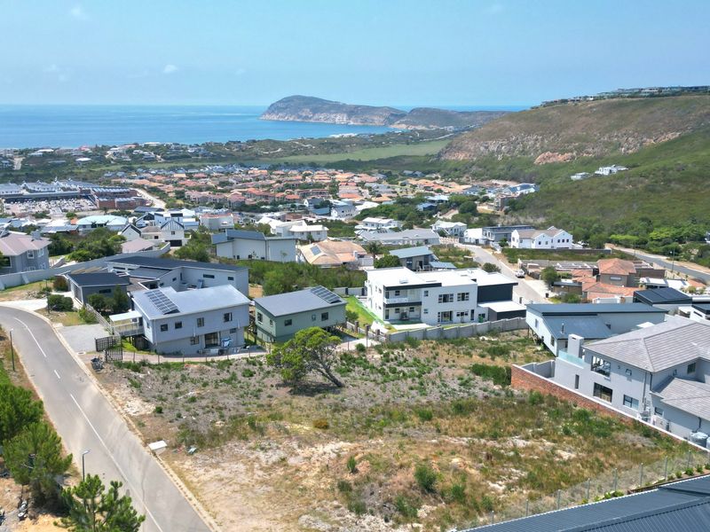An aerial view of a vacant residential plot situated within a developed coastal neighborhood, offering scenic views of the surrounding landscape and ocean.