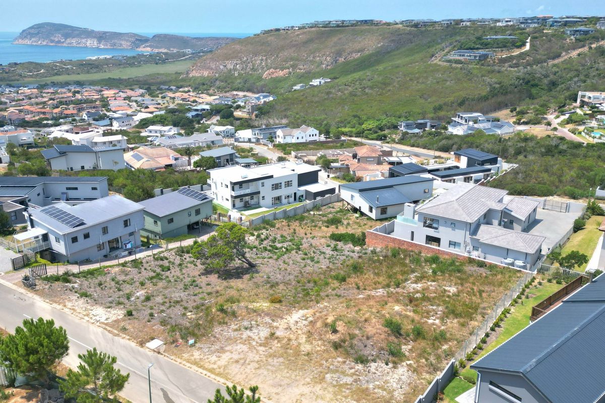 An elevated aerial view of a vacant residential plot situated in a developed coastal estate, showcasing surrounding neighborhood infrastructure and landscape.