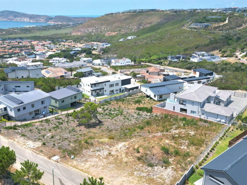 An elevated aerial view of a vacant residential plot situated in a developed coastal estate, showcasing surrounding neighborhood infrastructure and landscape.