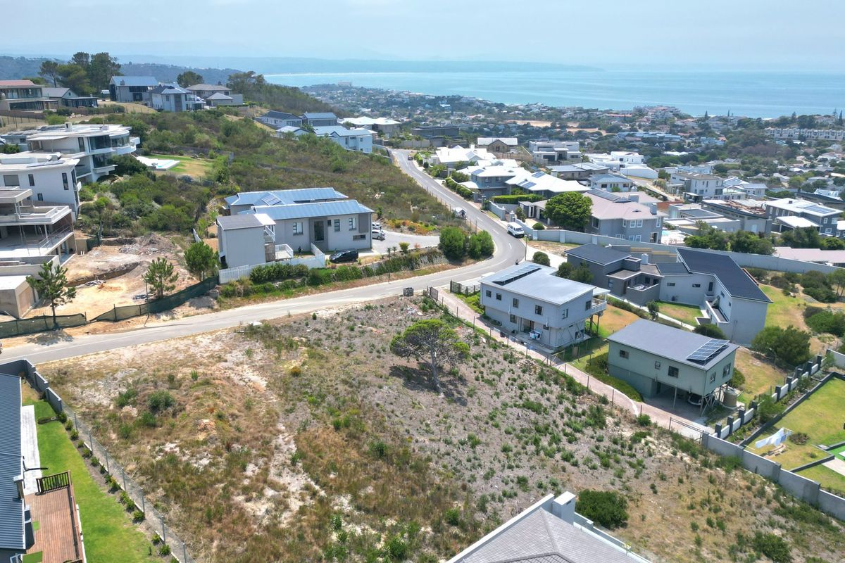 An aerial view of a vacant residential plot situated in a developed coastal neighborhood with surrounding homes and ocean views.
