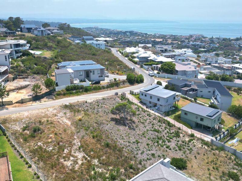 An aerial view of a vacant residential plot situated in a developed coastal neighborhood with surrounding homes and ocean views.
