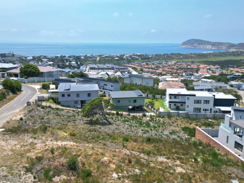 An aerial view of a vacant residential plot overlooking a coastal neighborhood and the ocean.