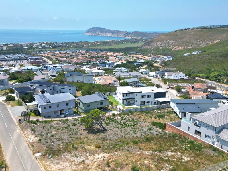 An aerial view of a vacant residential plot situated in a developed coastal neighborhood with surrounding homes and ocean views.