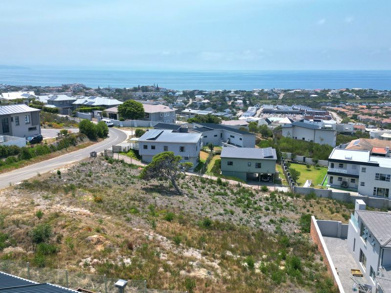 An aerial view of a vacant residential plot situated in a developed coastal neighborhood with surrounding homes and ocean views.