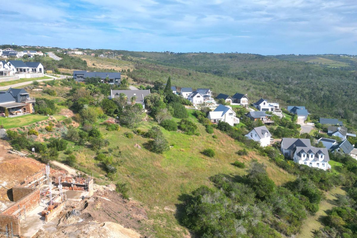 Aerial view of a residential estate featuring established homes and a vacant plot currently under construction on a sloped landscape.