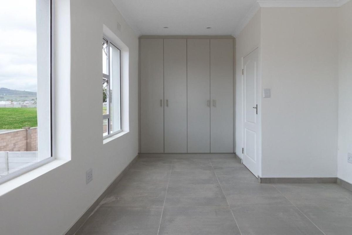 A bright, empty bedroom featuring neutral tiled flooring, built-in cupboards, and large windows providing natural light.