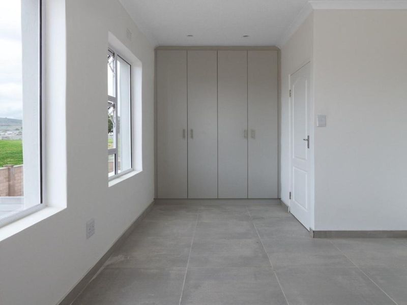 A bright, empty bedroom featuring neutral tiled flooring, built-in cupboards, and large windows providing natural light.