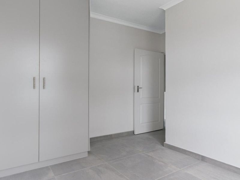 A clean, neutral bedroom featuring modern grey floor tiles and built-in cupboards, offering a blank canvas for personalization.