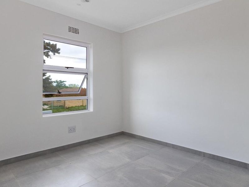 A clean, empty bedroom featuring neutral tiled flooring, crisp white walls, and a functional top-hung window providing natural light.