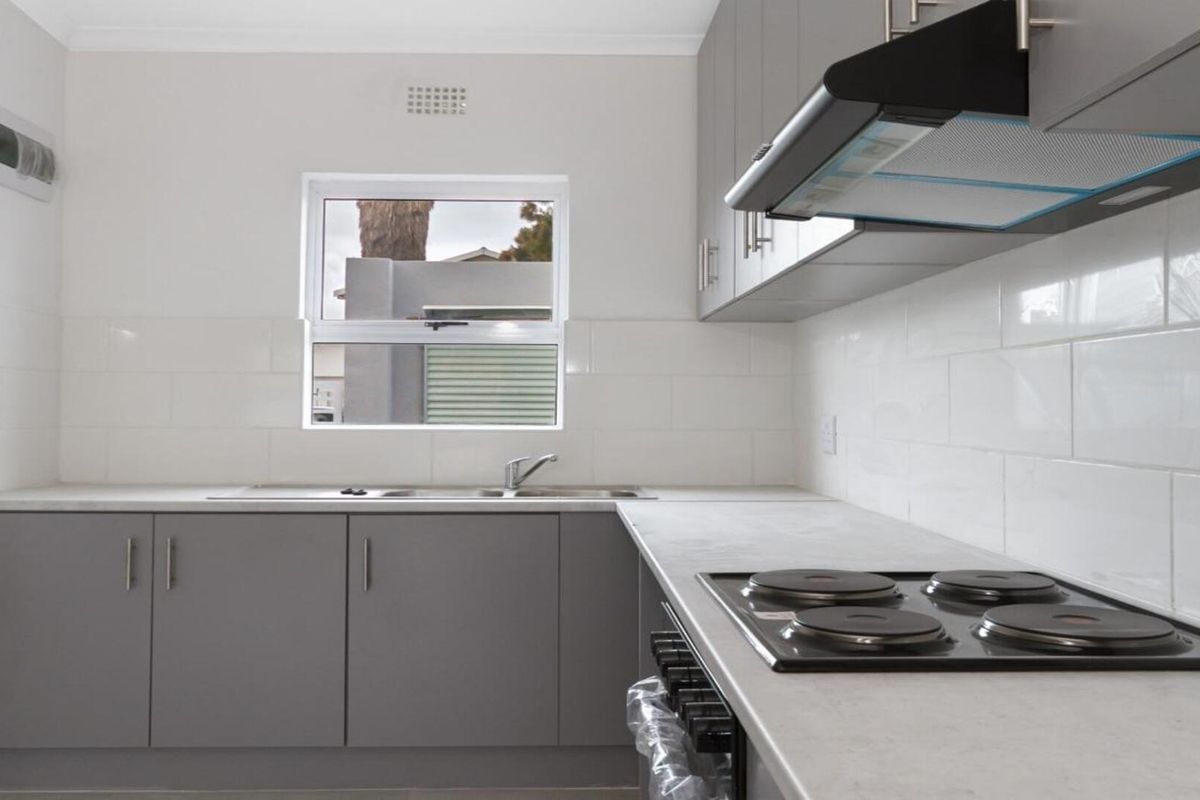 A clean, modern kitchen featuring grey cabinetry, white subway tile backsplash, built-in electric hob, extractor fan, and a stainless steel sink.