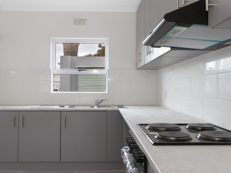 A clean, modern kitchen featuring grey cabinetry, white subway tile backsplash, built-in electric hob, extractor fan, and a stainless steel sink.