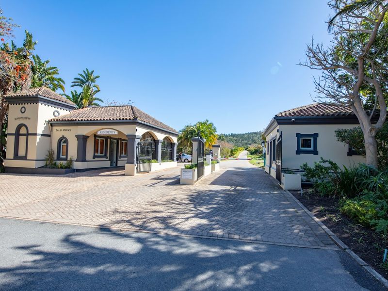 The entrance to the residential estate features a well-maintained security gatehouse, paved driveway, and established landscaping, providing a secure and welcoming access point.