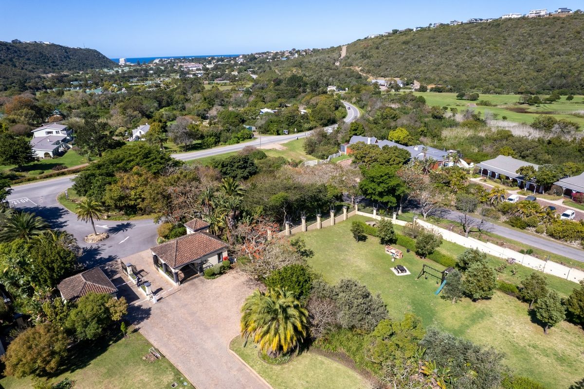 Aerial view of a residential property featuring a gated entrance, paved driveway, and expansive landscaped garden within a scenic estate setting.