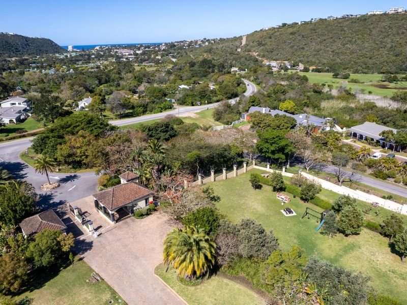 Aerial view of a residential property featuring a gated entrance, paved driveway, and expansive landscaped garden within a scenic estate setting.