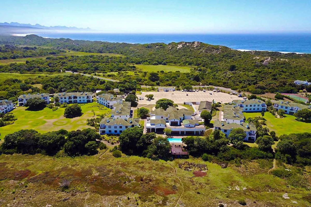 Aerial view of a coastal apartment complex featuring landscaped grounds, a swimming pool, and extensive parking facilities near the ocean.