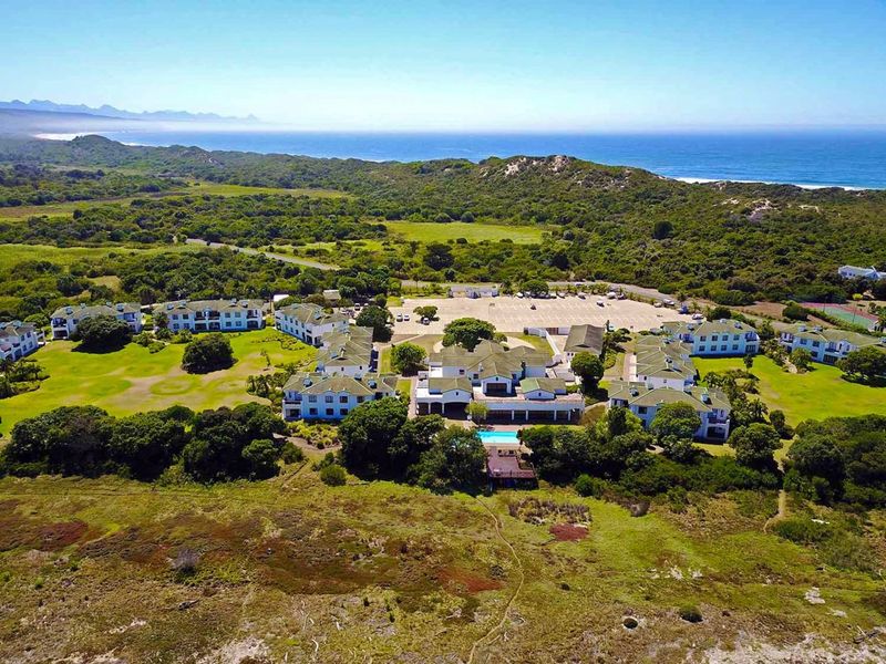 Aerial view of a coastal apartment complex featuring landscaped grounds, a swimming pool, and extensive parking facilities near the ocean.