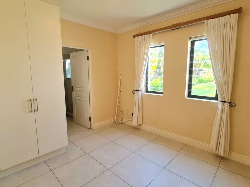 A bright, empty bedroom featuring neutral tiled flooring, built-in wardrobes, and dual windows with garden views.