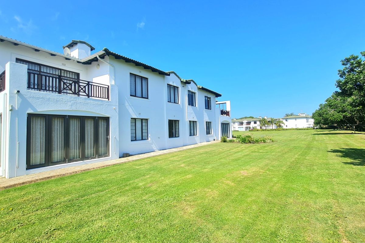 Rear view of a multi-story apartment building featuring white exterior walls, a tiled roof, balconies, and extensive well-maintained lawn areas.