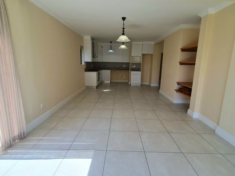 Spacious open-plan living and kitchen area featuring tiled floors, built-in cabinetry, integrated appliances, and direct access to the garden through a sliding glass door.