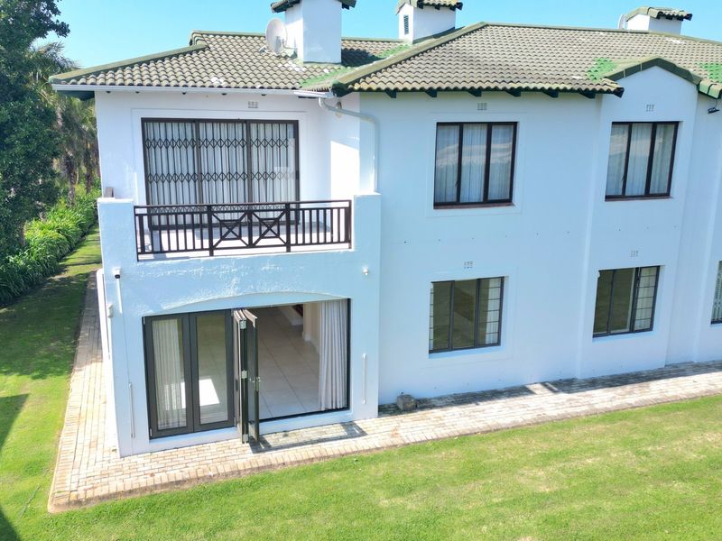 Aerial view of the rear elevation of a two-story apartment building featuring a balcony, paved garden path, and white exterior walls.