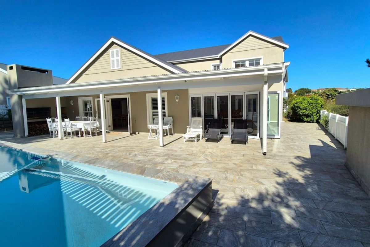 Rear exterior view featuring a covered patio, stone paved pool deck, and a built-in braai area, perfect for outdoor entertaining.