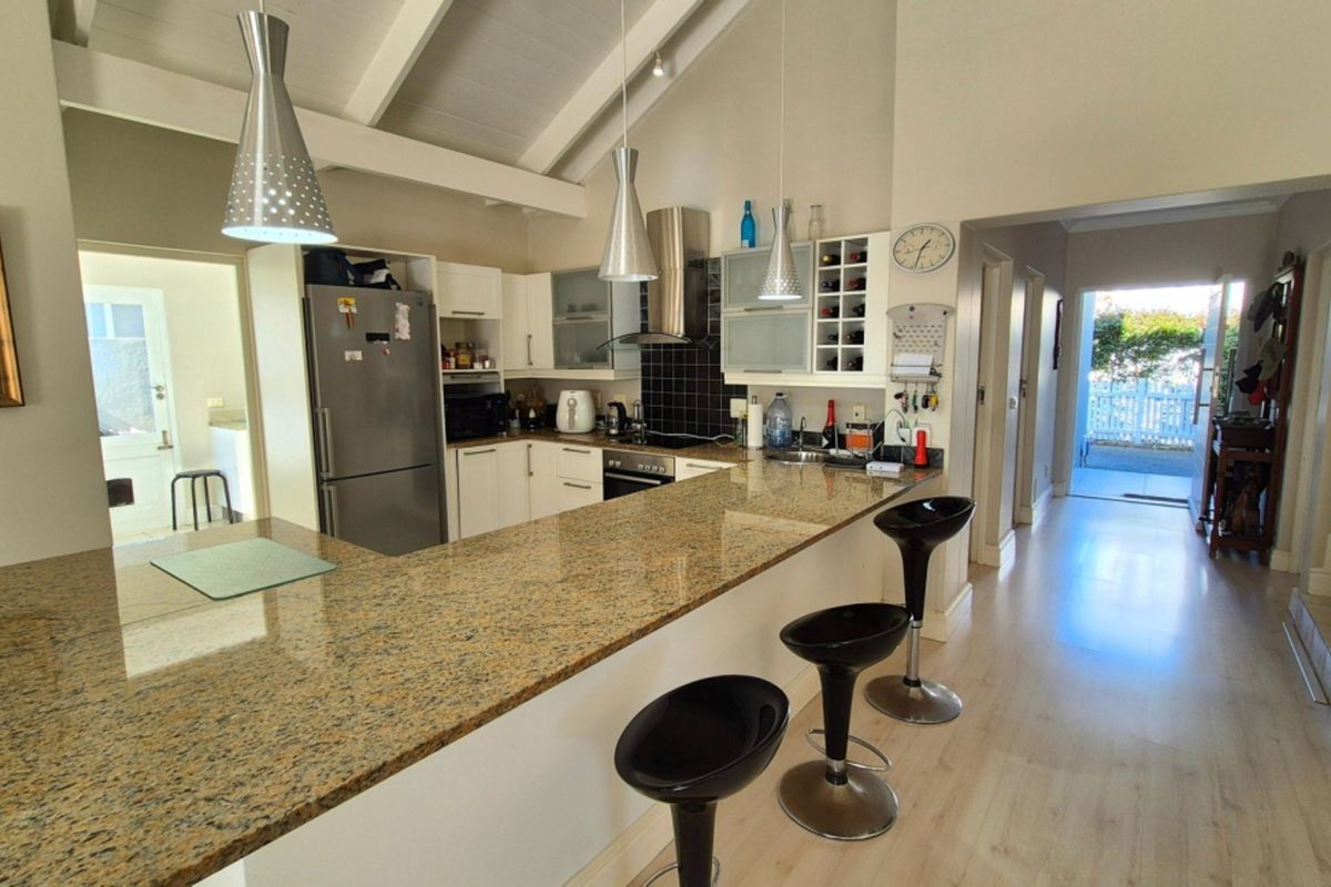 A functional kitchen featuring granite countertops, built-in cabinetry, a hob with extractor fan, and a breakfast bar, set under a vaulted ceiling with exposed beams.