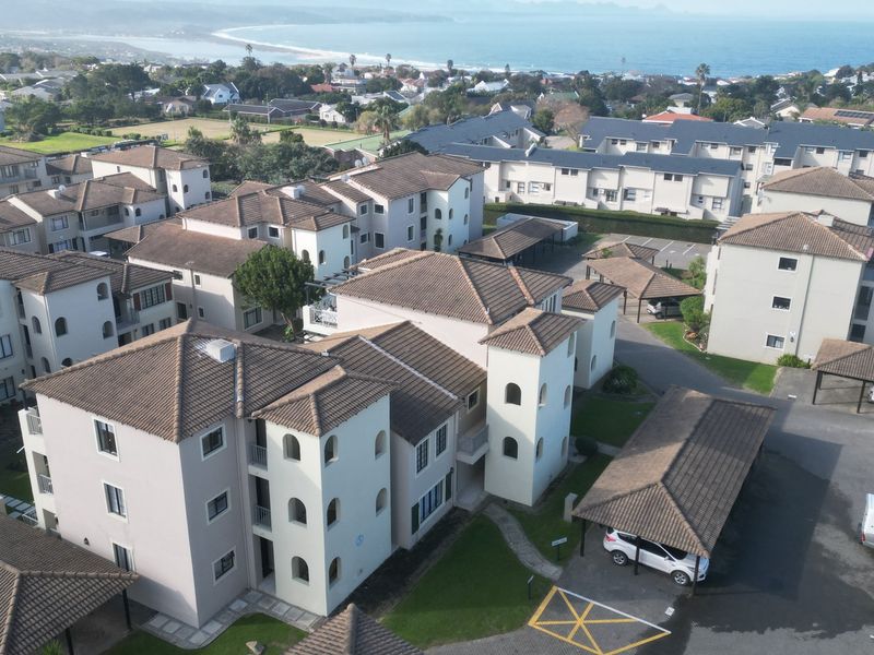 Aerial view of a residential apartment complex featuring multiple buildings with tiled roofs, paved parking areas, and covered carports.