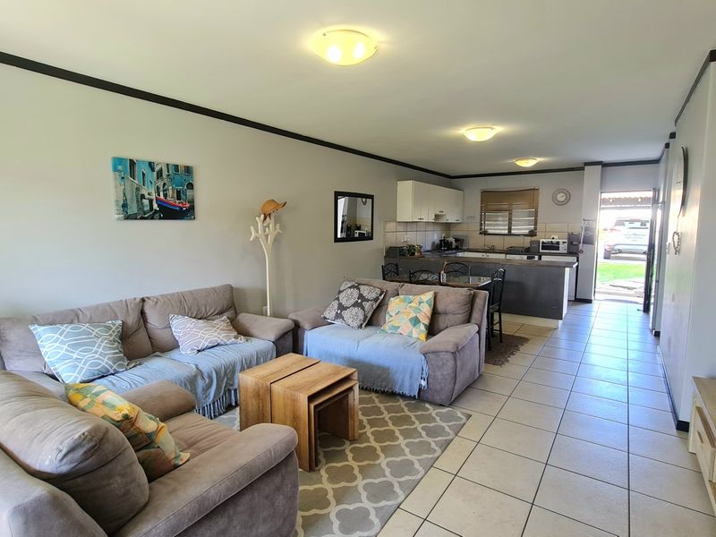 Open-plan living and kitchen area featuring tiled flooring, neutral wall tones, and functional kitchen cabinetry with a breakfast counter.