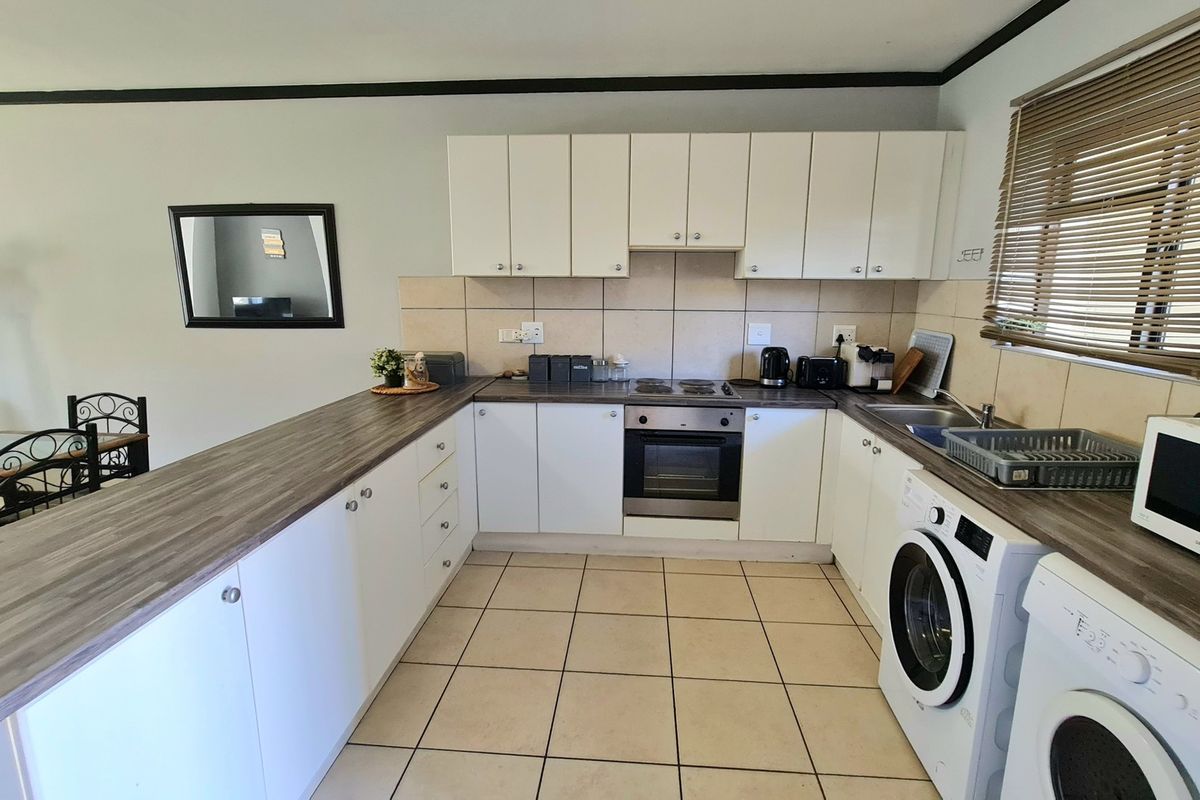 Functional kitchen featuring white cabinetry, laminate countertops, integrated oven and hob, tiled backsplash, and dedicated space for laundry appliances.