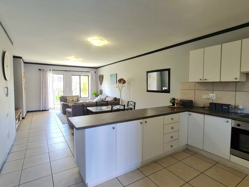 Open-plan living area featuring a functional kitchen with built-in cabinetry, oven, and hob, flowing into a bright living space with access to a balcony.