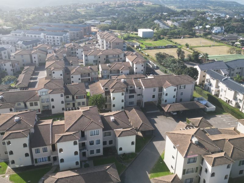 An aerial view of a residential apartment complex featuring multiple multi-story buildings with tiled roofs, paved driveways, and covered parking areas.